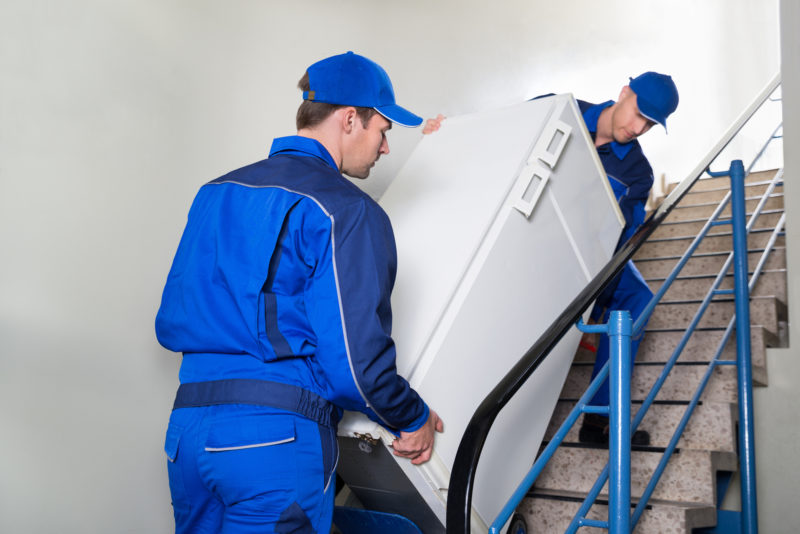 Movers moving a refrigerator down stairs into a storage unit